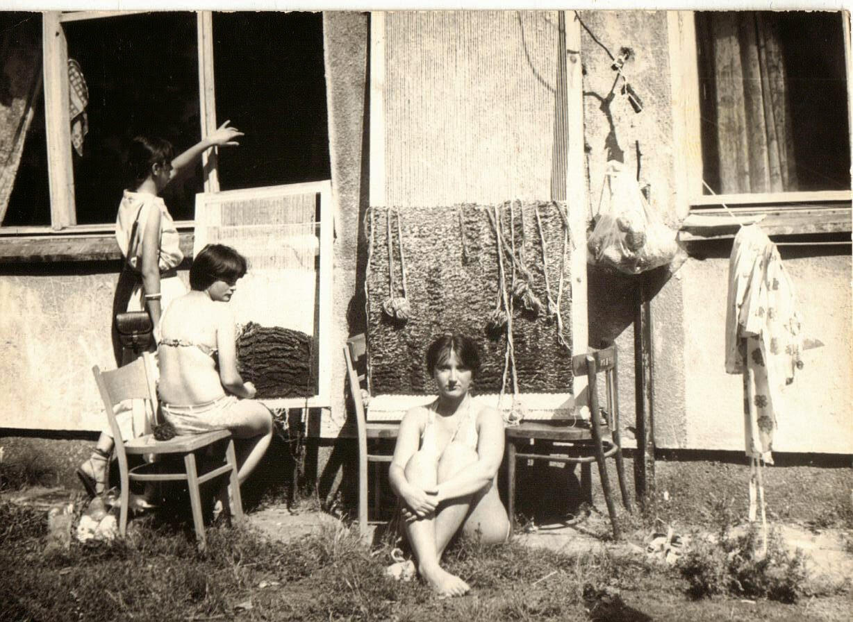 Renata (Far Left) standing talking to other students inside the classroom while beside a couple students making textile art outdoors. School took advantage of the lighting,.